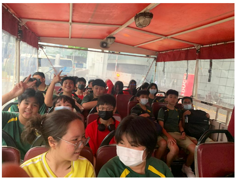 Group of children wearing face masks seated inside a red open-top tour bus.